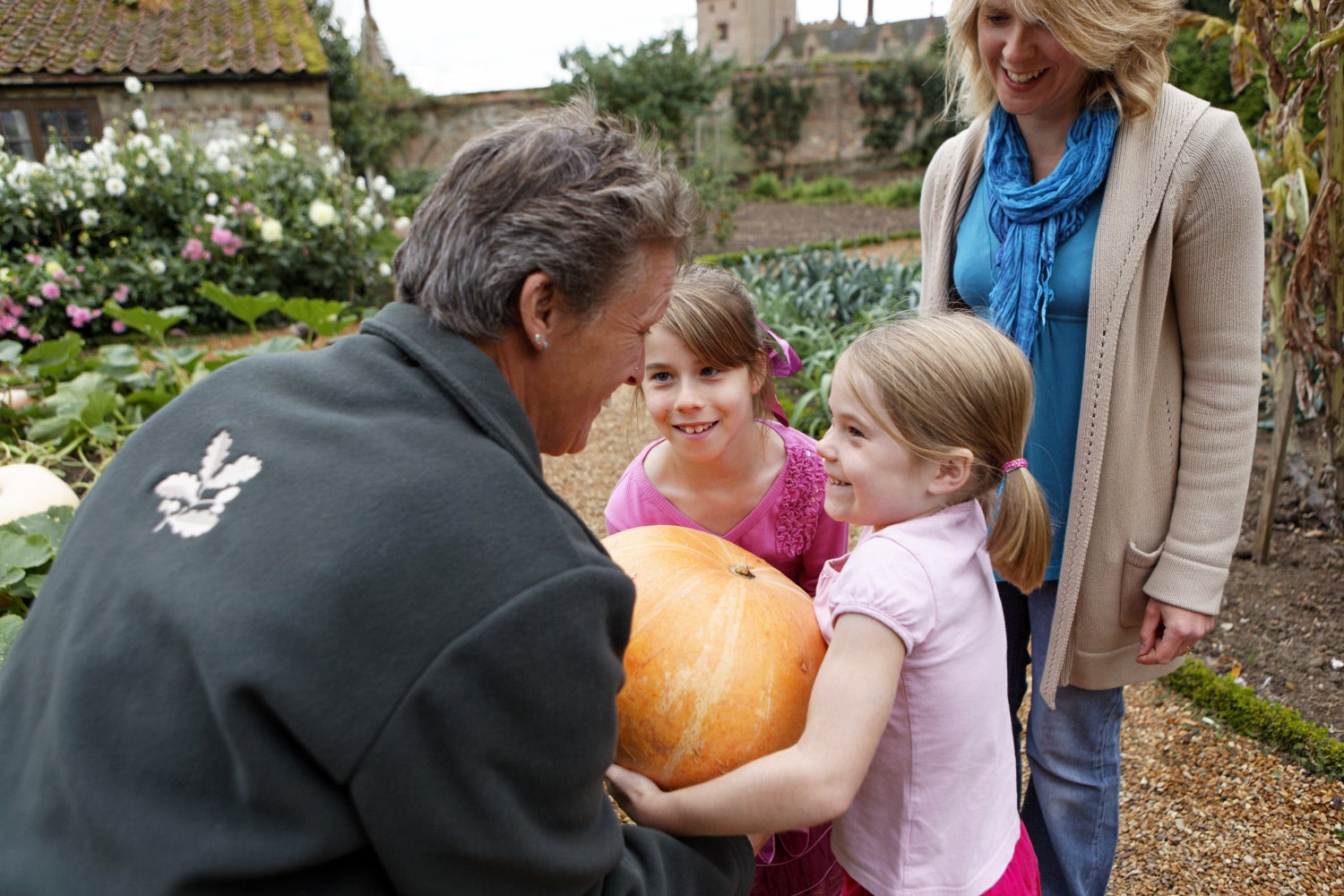 A woman and two children are in the kitchen garden holding a large pumpkin.