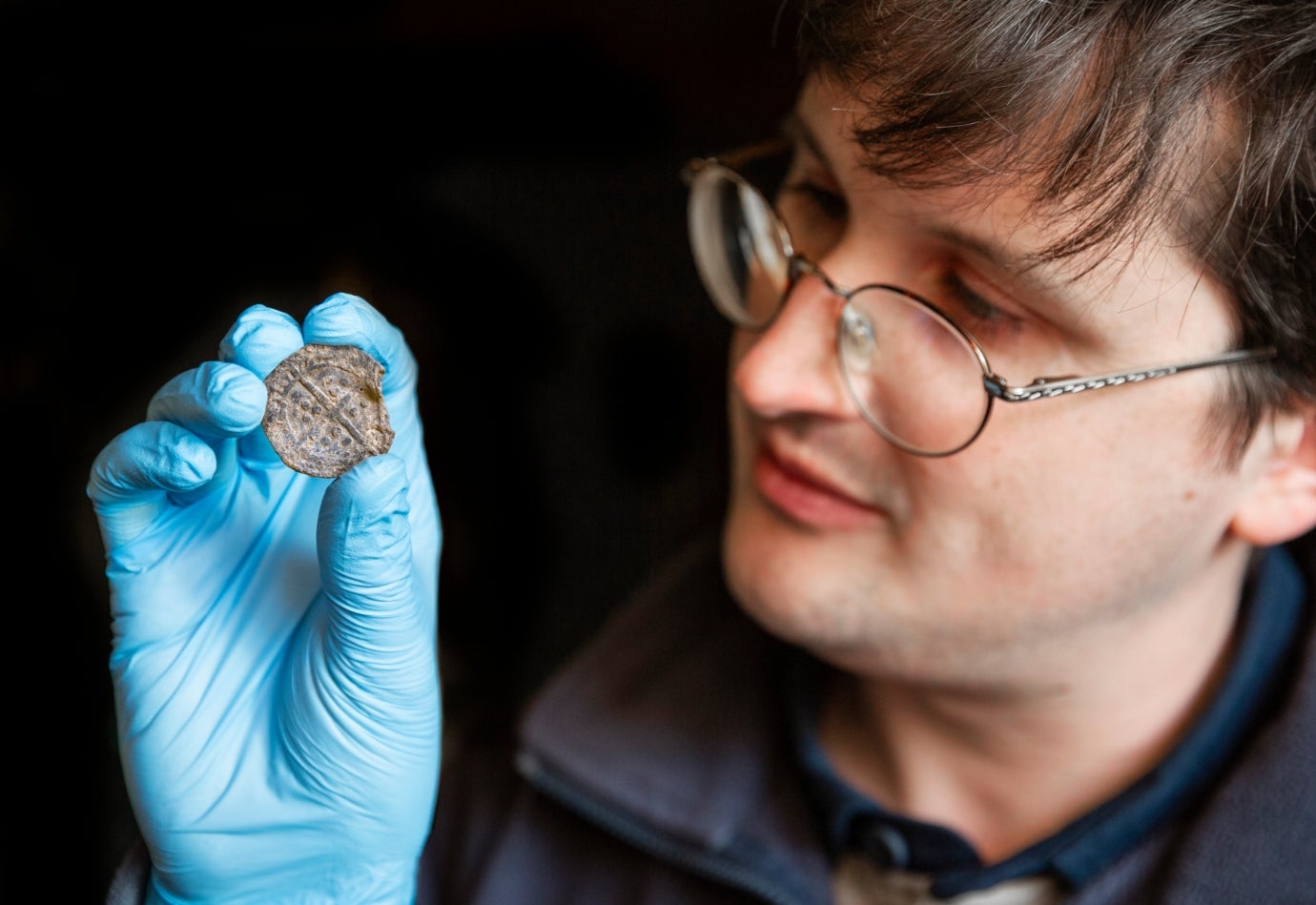 A member of the National Trust conservation team is holding up a medieval Boy Bishop token. Its the size of a 2 pence piece and has indentations on the surface.