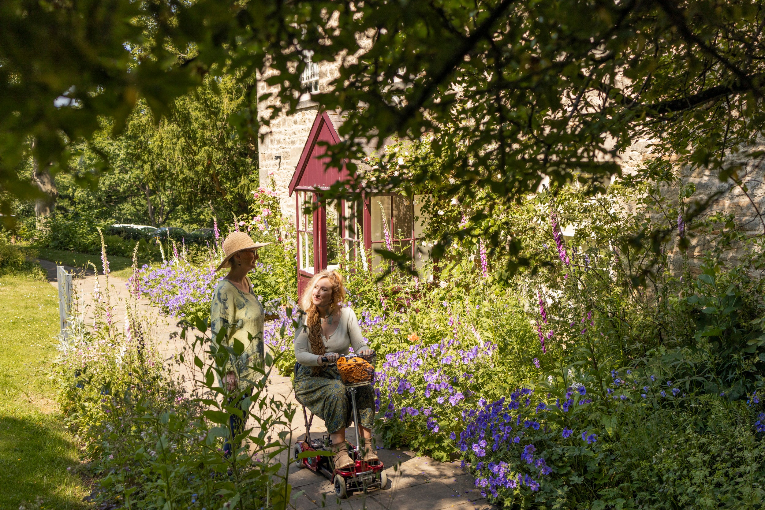 Two women in the garden in front of the Cherryburn museum. One is riding a mobility scooter/