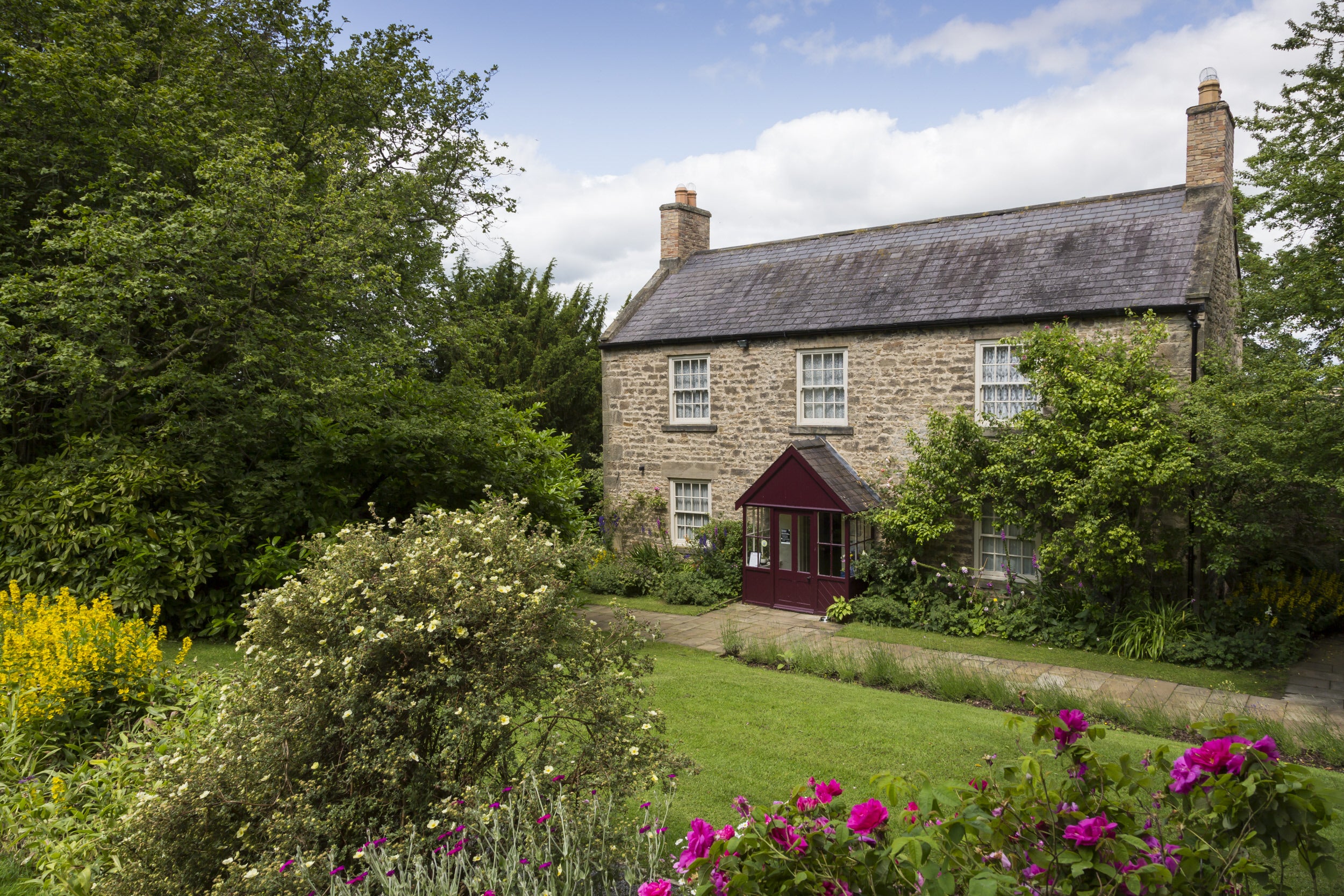 Cherryburn farmhouse with lawn in front and framed by trees and plants