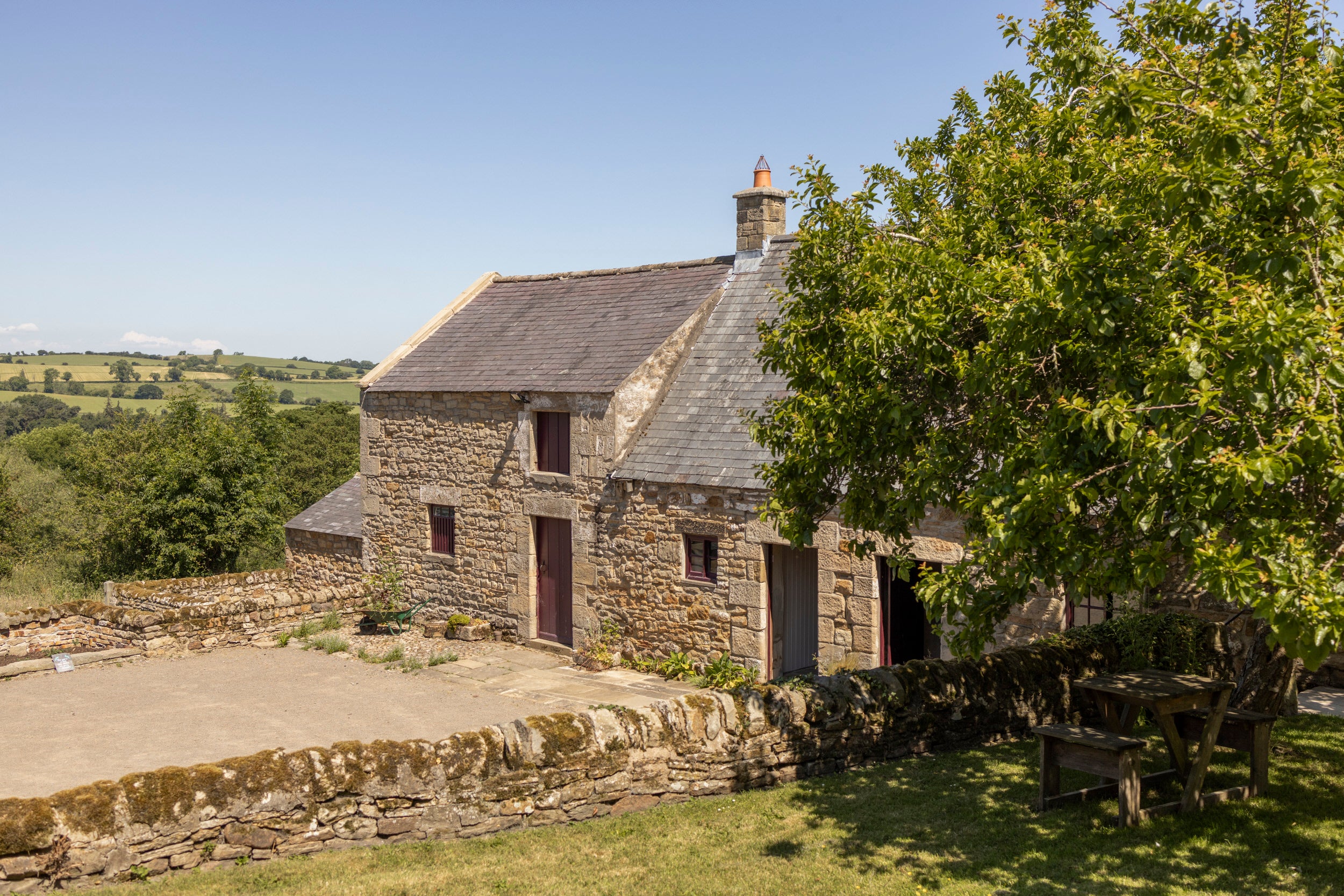 An 18th century stone cottage with a farmyard in front and surrounded by trees and green fields
