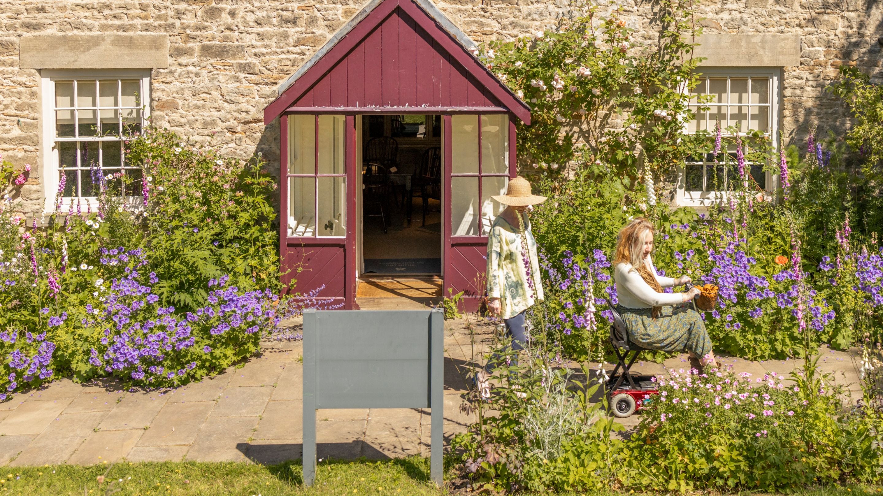 Visitors exploring plants in the farmhouse garden at Cherryburn, Northumberland with a porch and windows of a building in the background