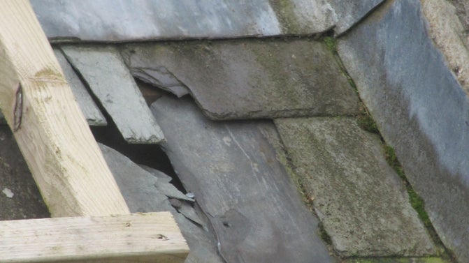 A cracked grey, slate ridge tile has created a gap in the roof.