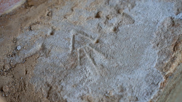 Close-up of a mason's mark etched into a sandstone block. The carving resembles a small rocket shape and is visible on the weathered stone surface.
