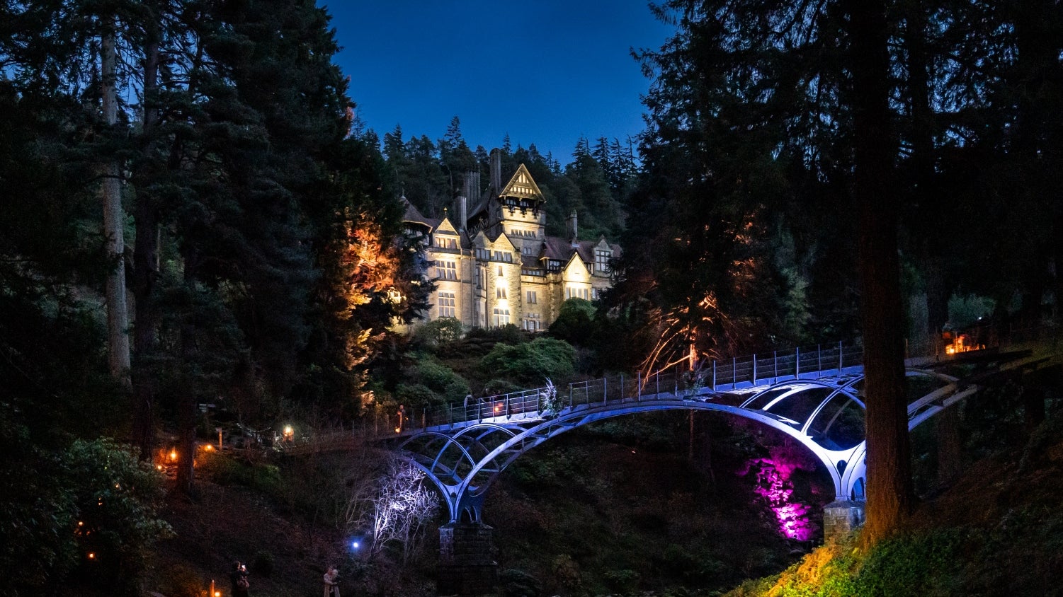 The House and Iron Bridge illuminated in colourful lights during Christmas at Cragside 2024.