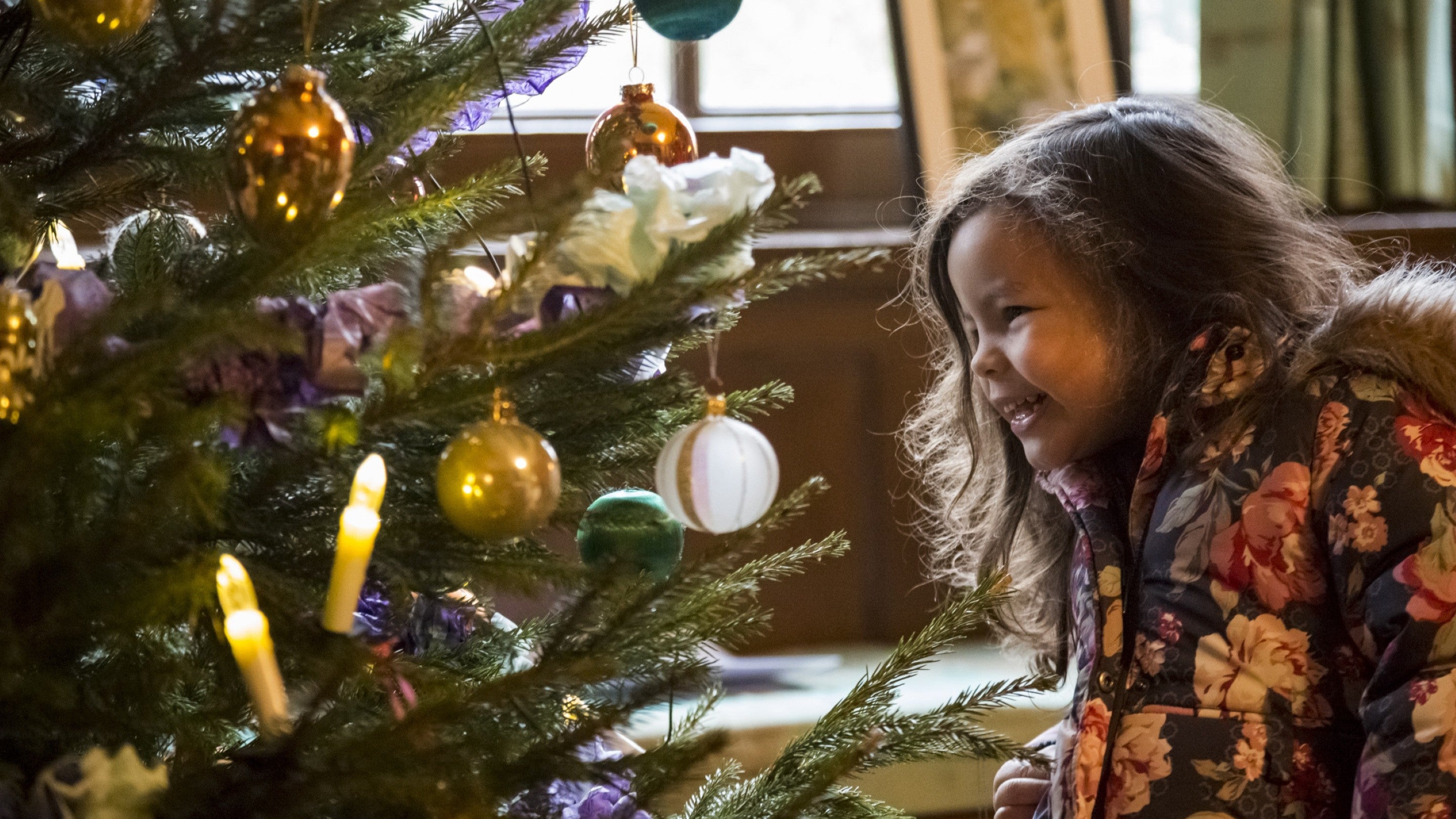 A young girl looking at a large white bauble on a Christmas tree.