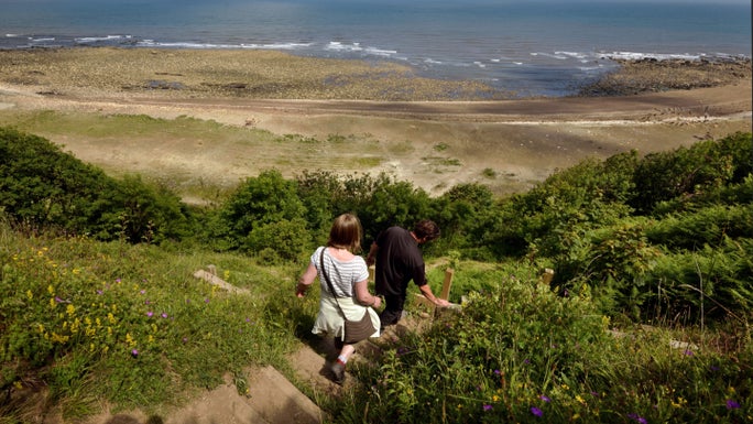 Two people heading down steep steps down the cliff towards a sandy beach.