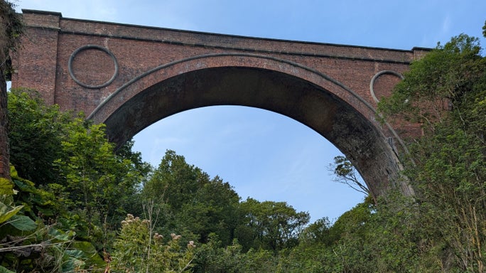 View of a large red brick archway and lots of greenery.