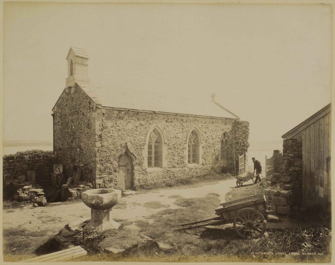 Historical image of a man pushing a wheelbarrow, walking past St Cuthbert's Chapel on the Farne Islands.