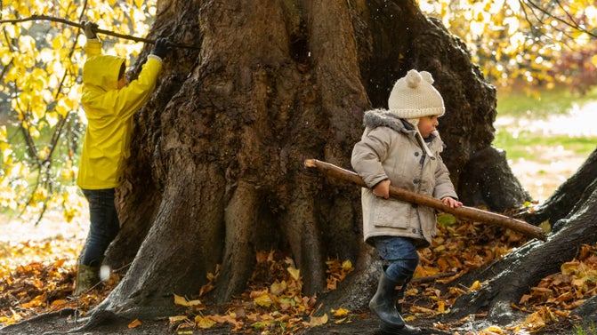 Two small children moving branches to build a den among autumn leaves