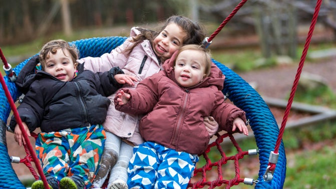 Three young children laughing on the bucket swing