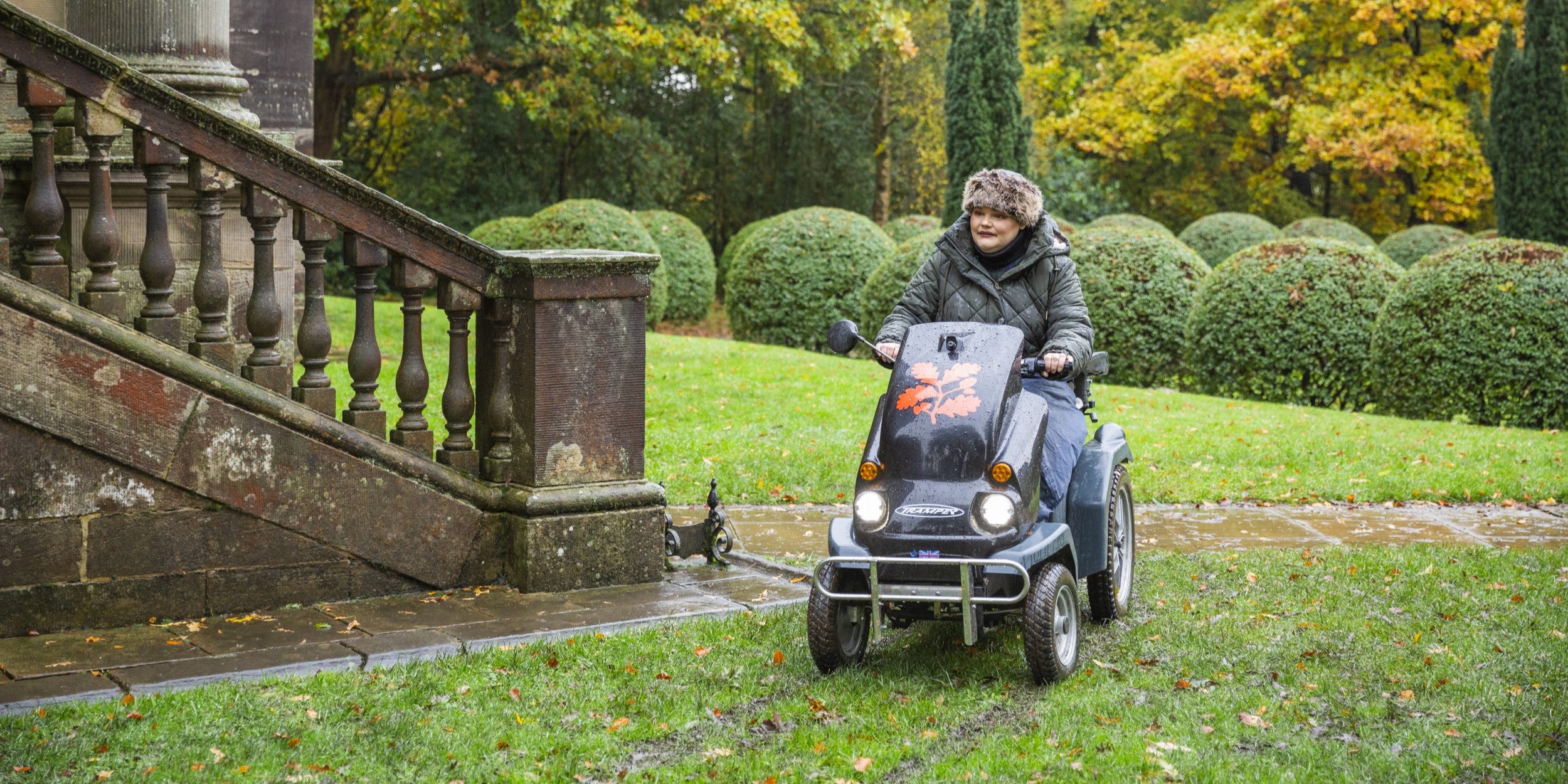 Visitor on a mobility Tramper with autumn leaves and stairs in the background.