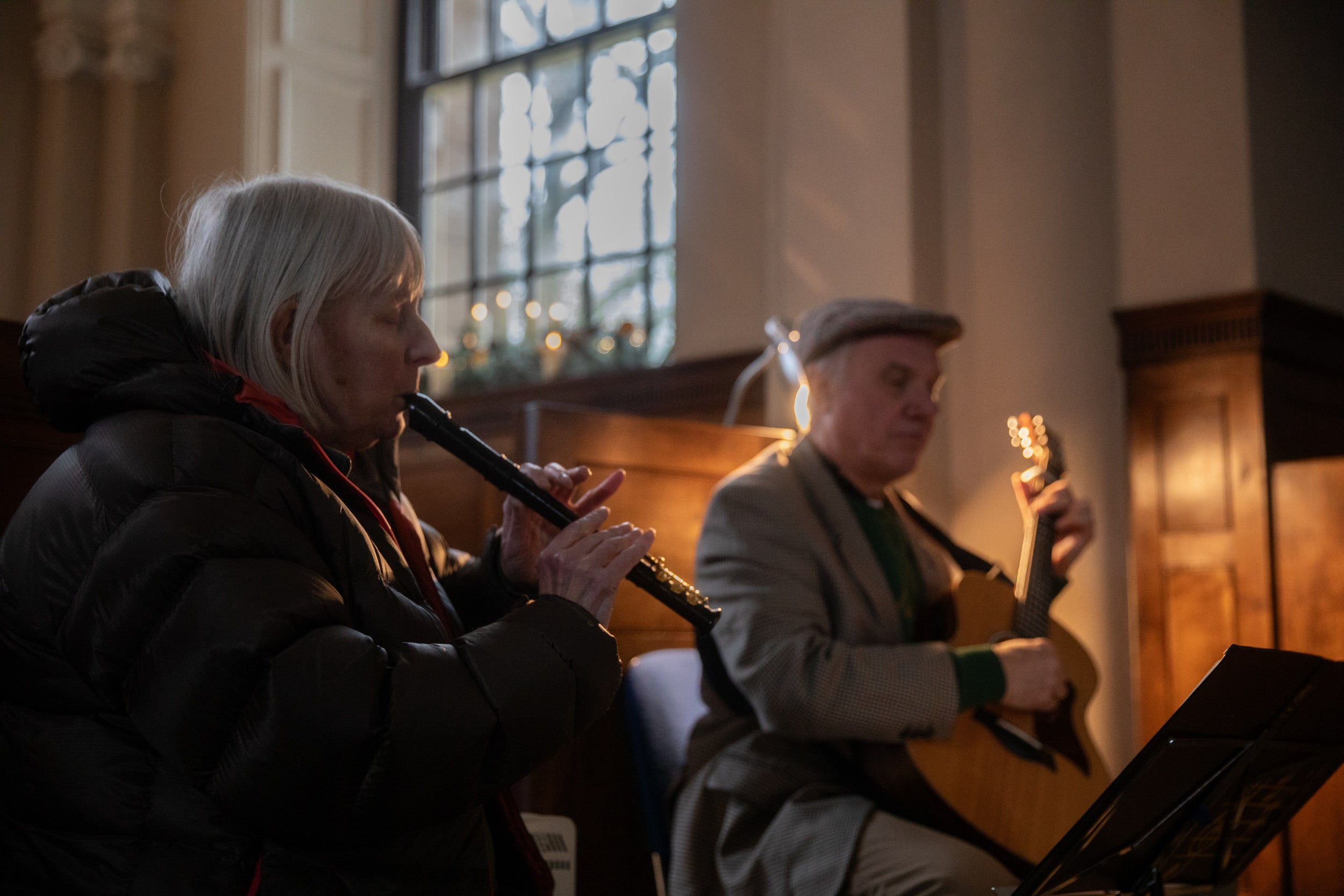 A woman playing recorder and a man playing guitar in soft lighting.
