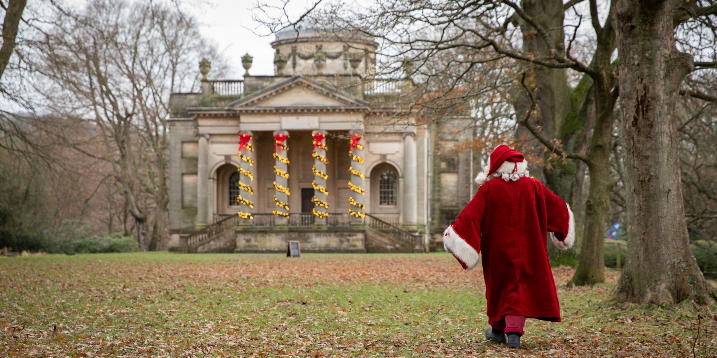 Father Christmas in his traditional red coat walking towards Gibside Chapel, with the column decorated with lights.