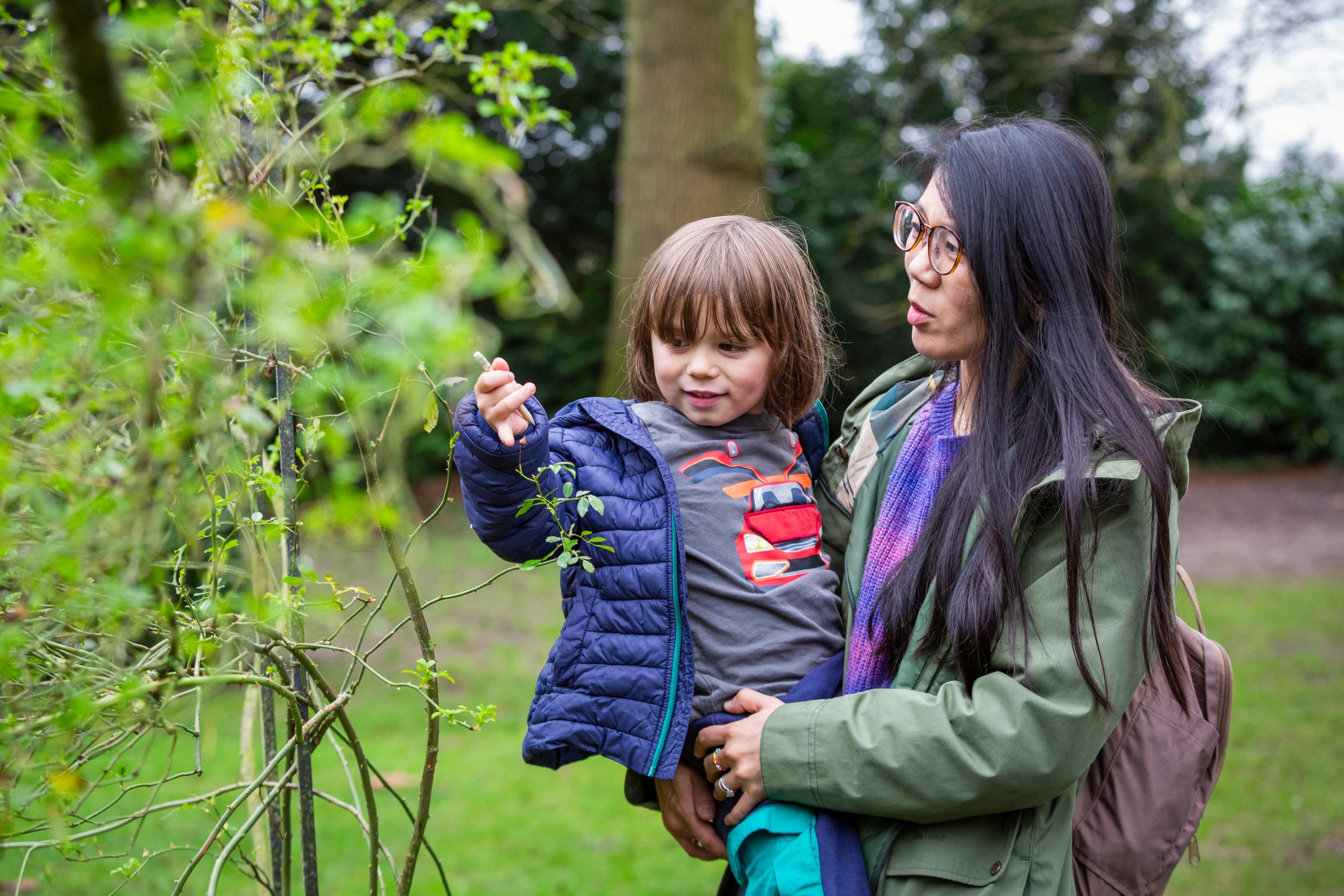 Woman holds a small child looking at leaf.