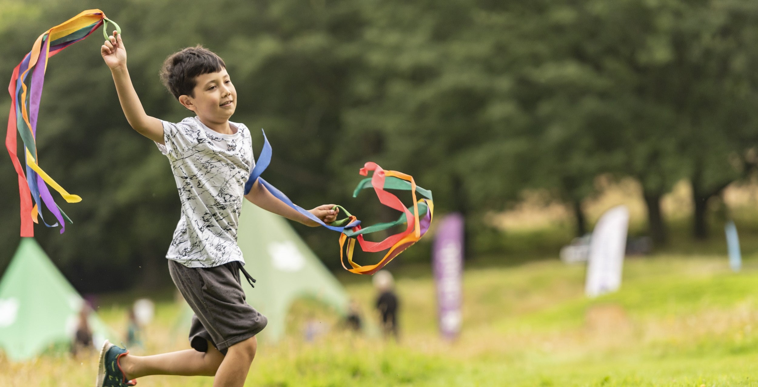 Boy waving around ribbons on the grass.