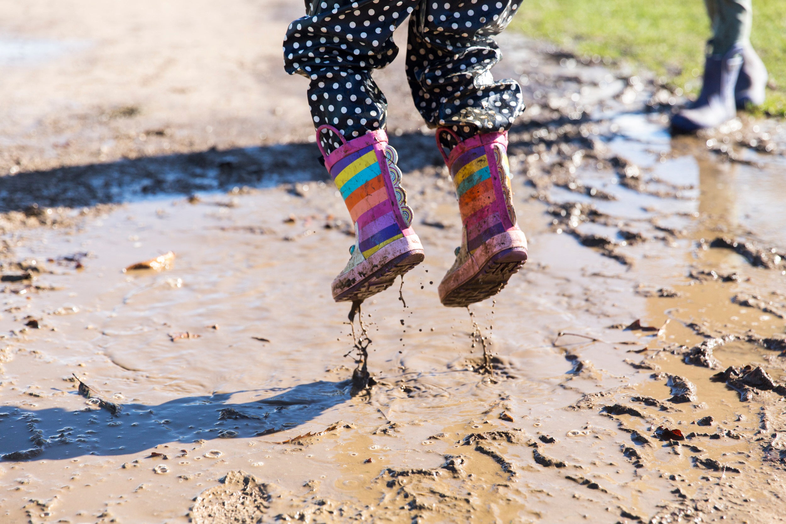Child jumping in wellies above a muddy puddle.