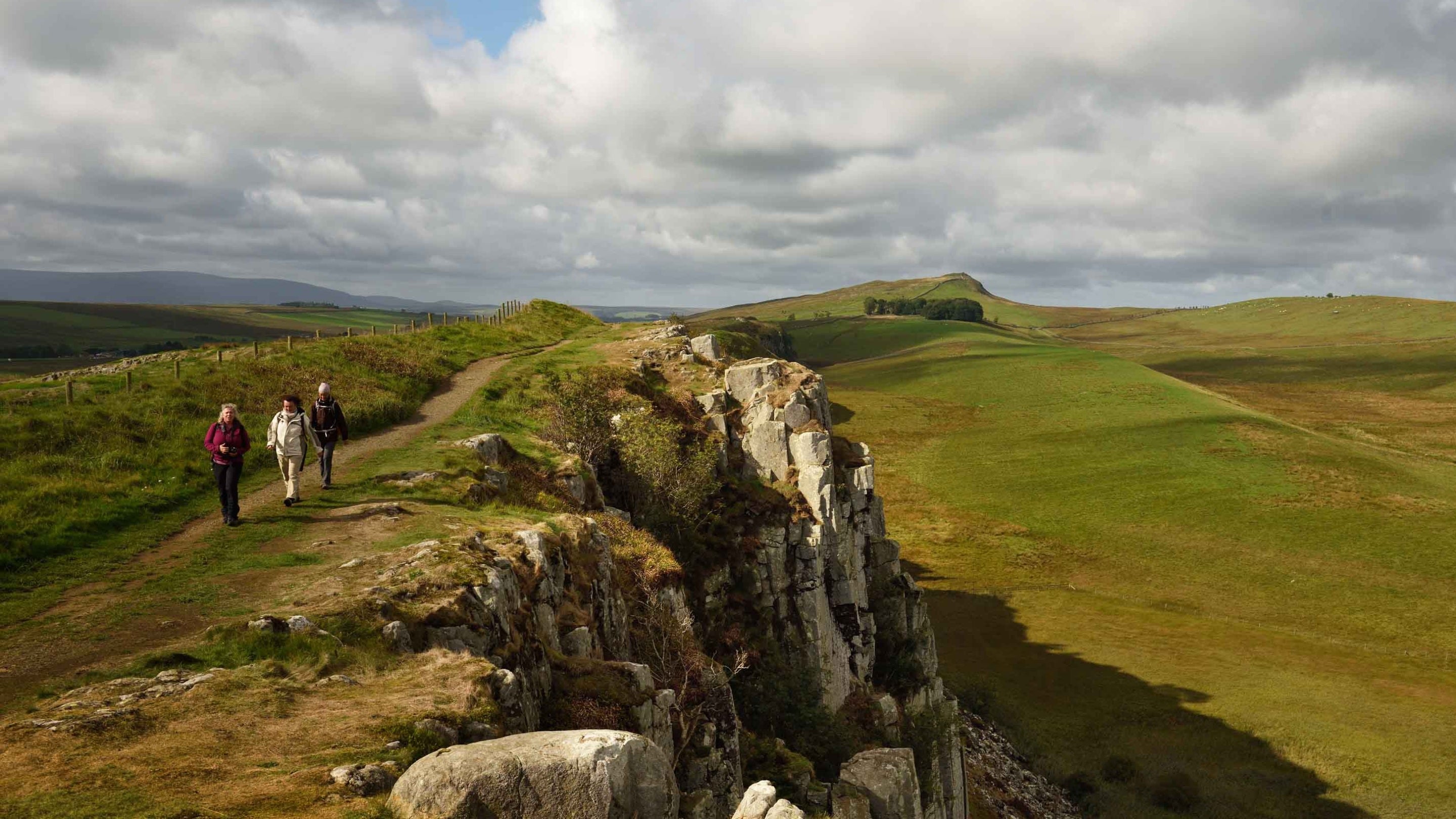 Visitors walking on the path beside the wall at Hadrian's Wall and Housesteads Fort, Northumberland