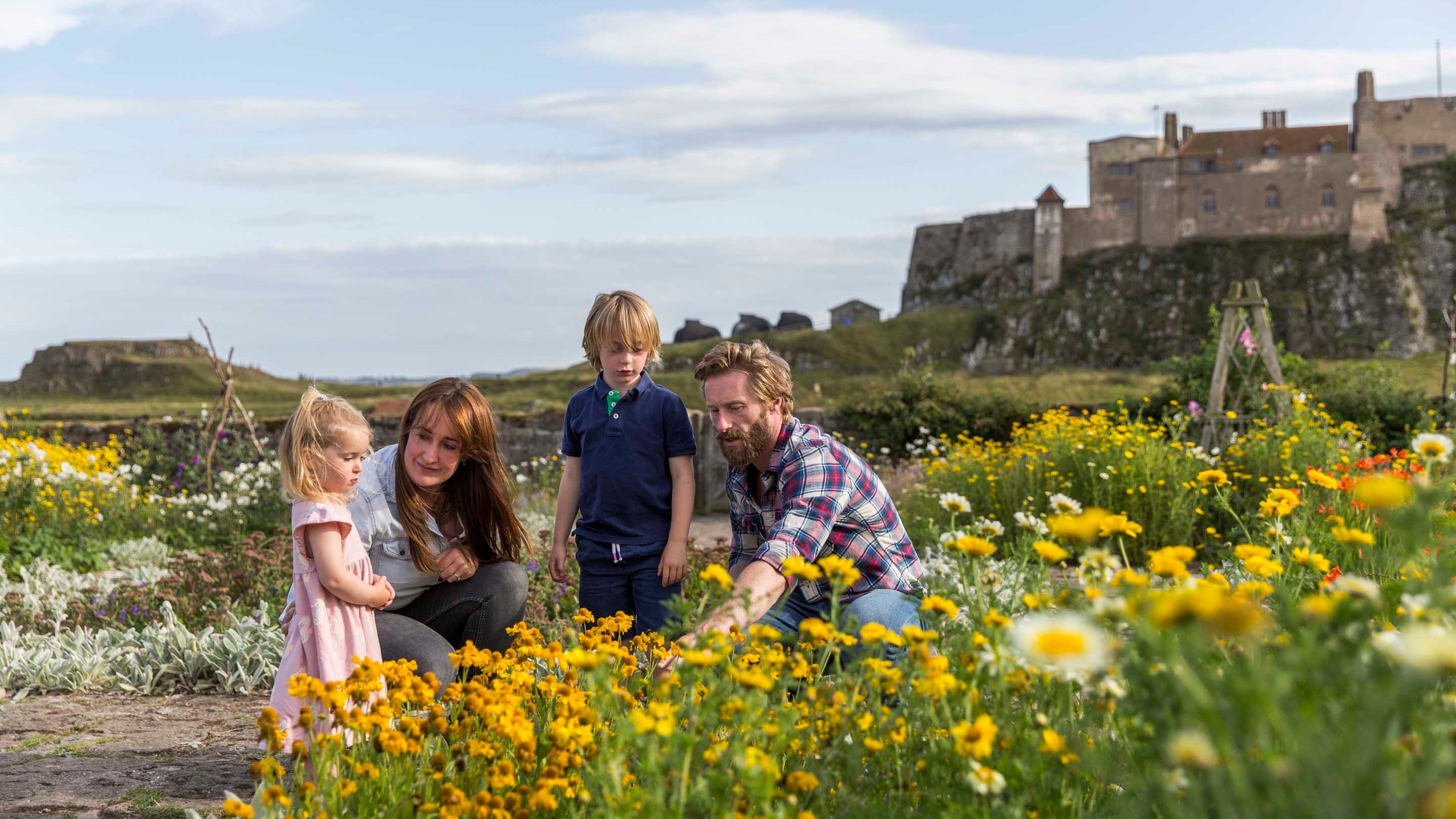Two adults and two children looking at flowers in a garden with Lindisfarne Castle behind them