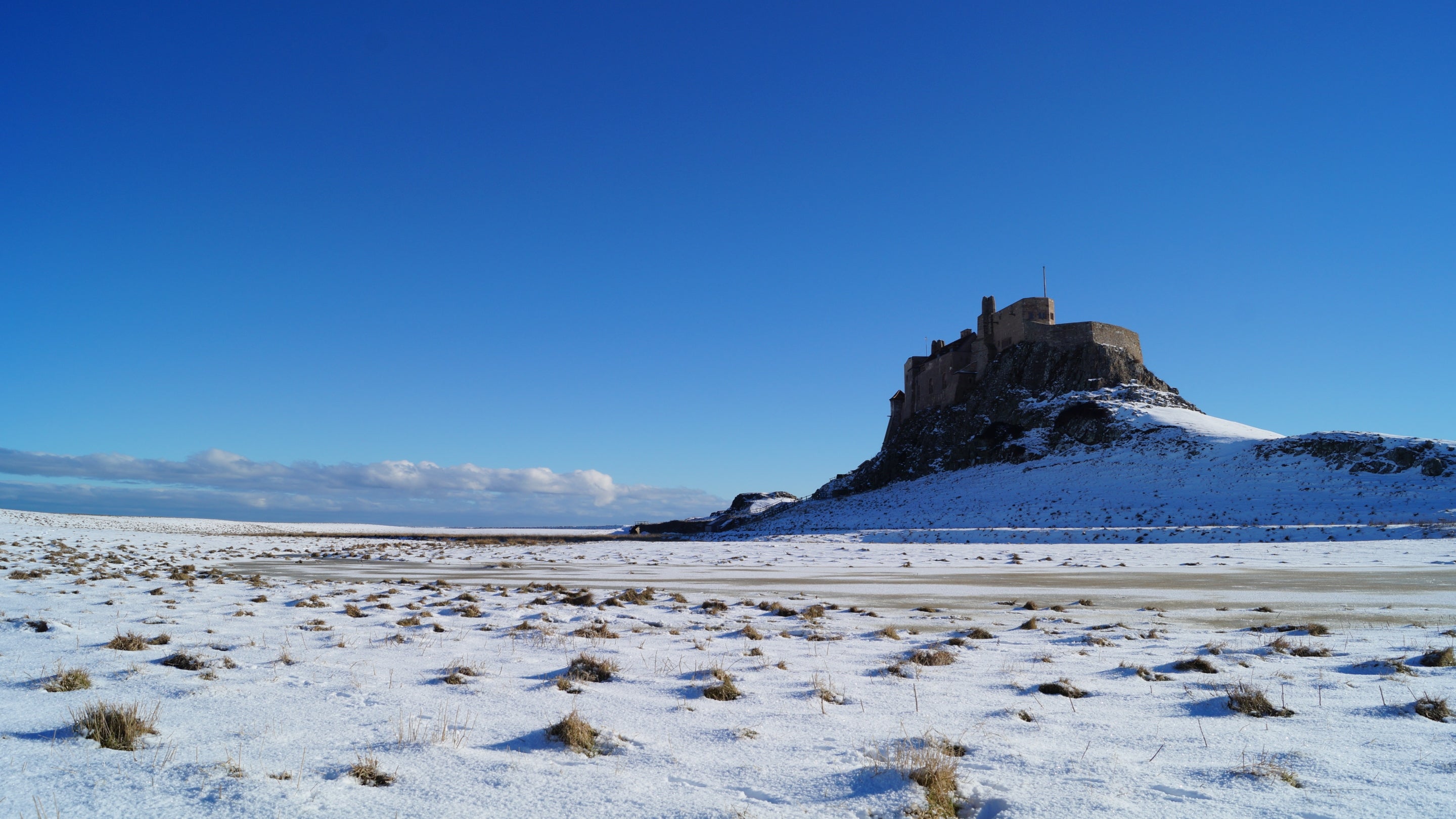 A picture showing Lindisfarne Castle on Holy Island, Northumberland following snowfall in the winter of 2021, with blue sky.