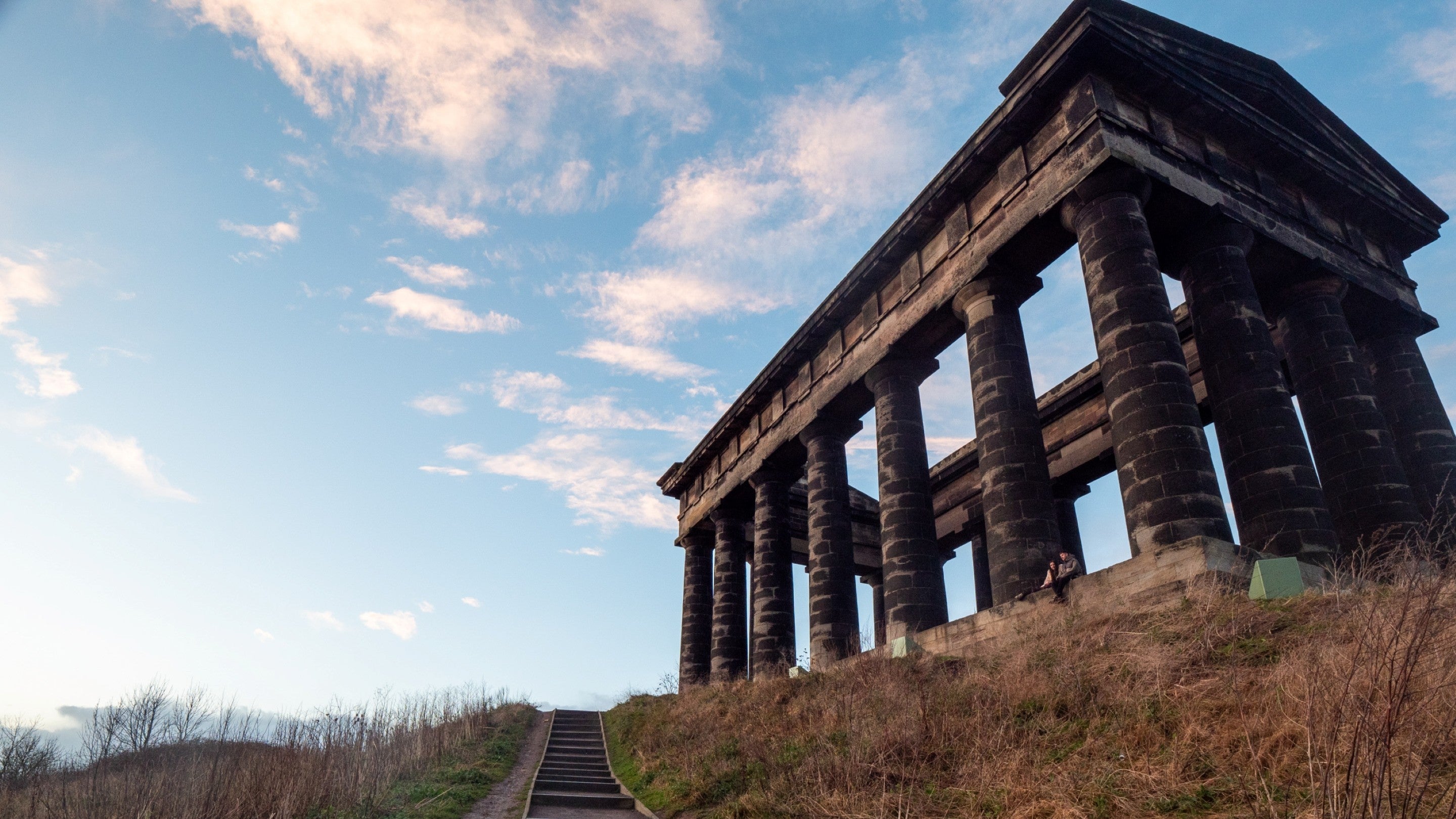 View of a large grey columned building at dusk with some wooden steps going up to it.
