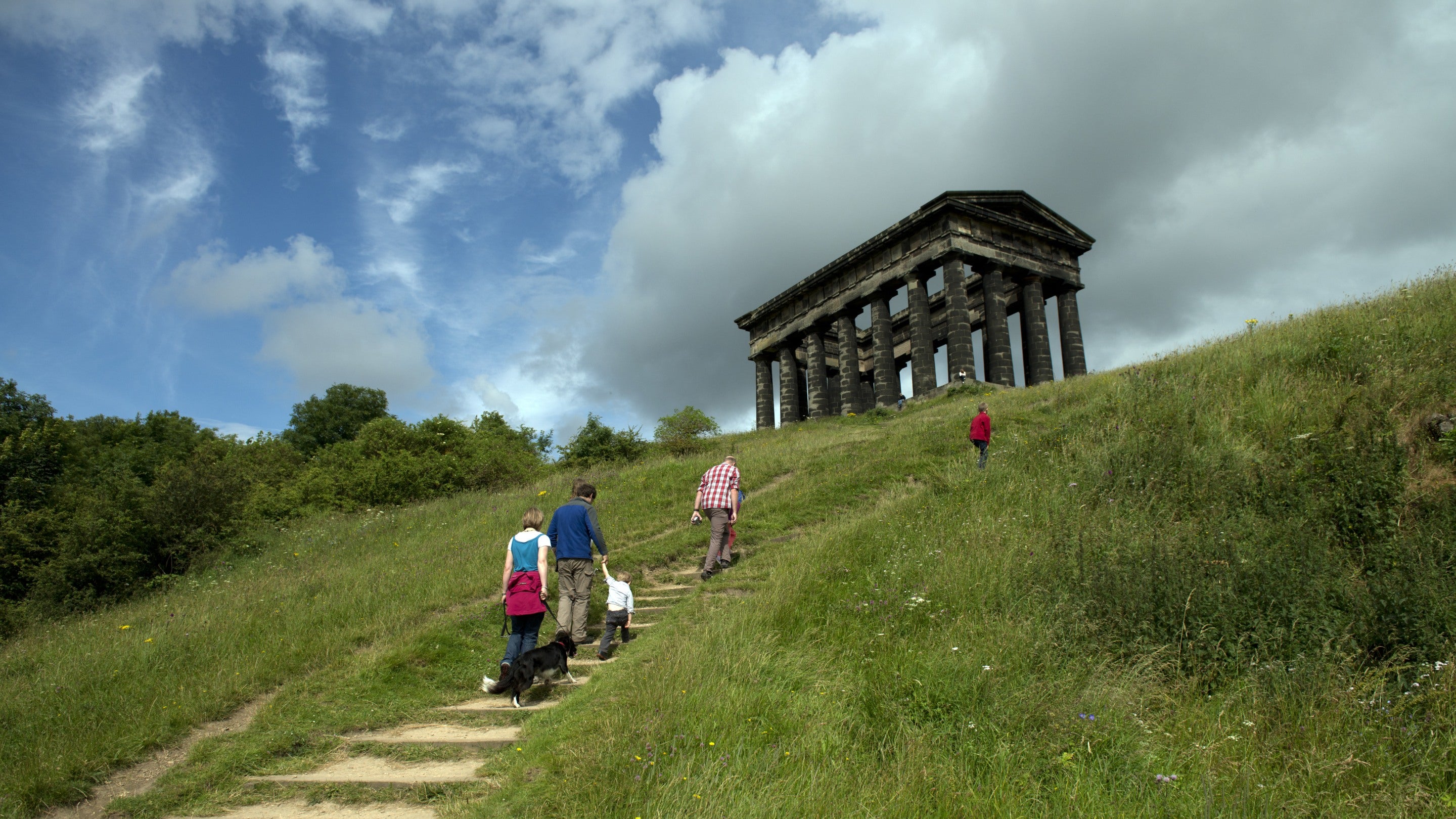 A group of visitors walk up steps towards the Penshaw Monument in the background on a sunny day, in Sunderland