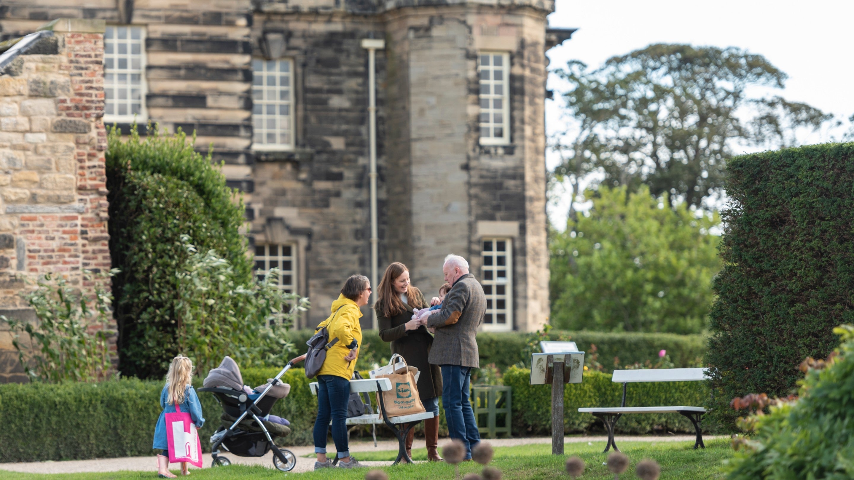 A family explores the gardens of Seaton Delaval Hall, Northumberland, during autumn with the exterior of Seaton Delaval Hall in the background