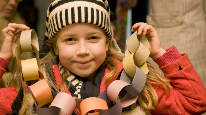A child in an orange coat and black and white striped bobble hat is holding up paper chains.