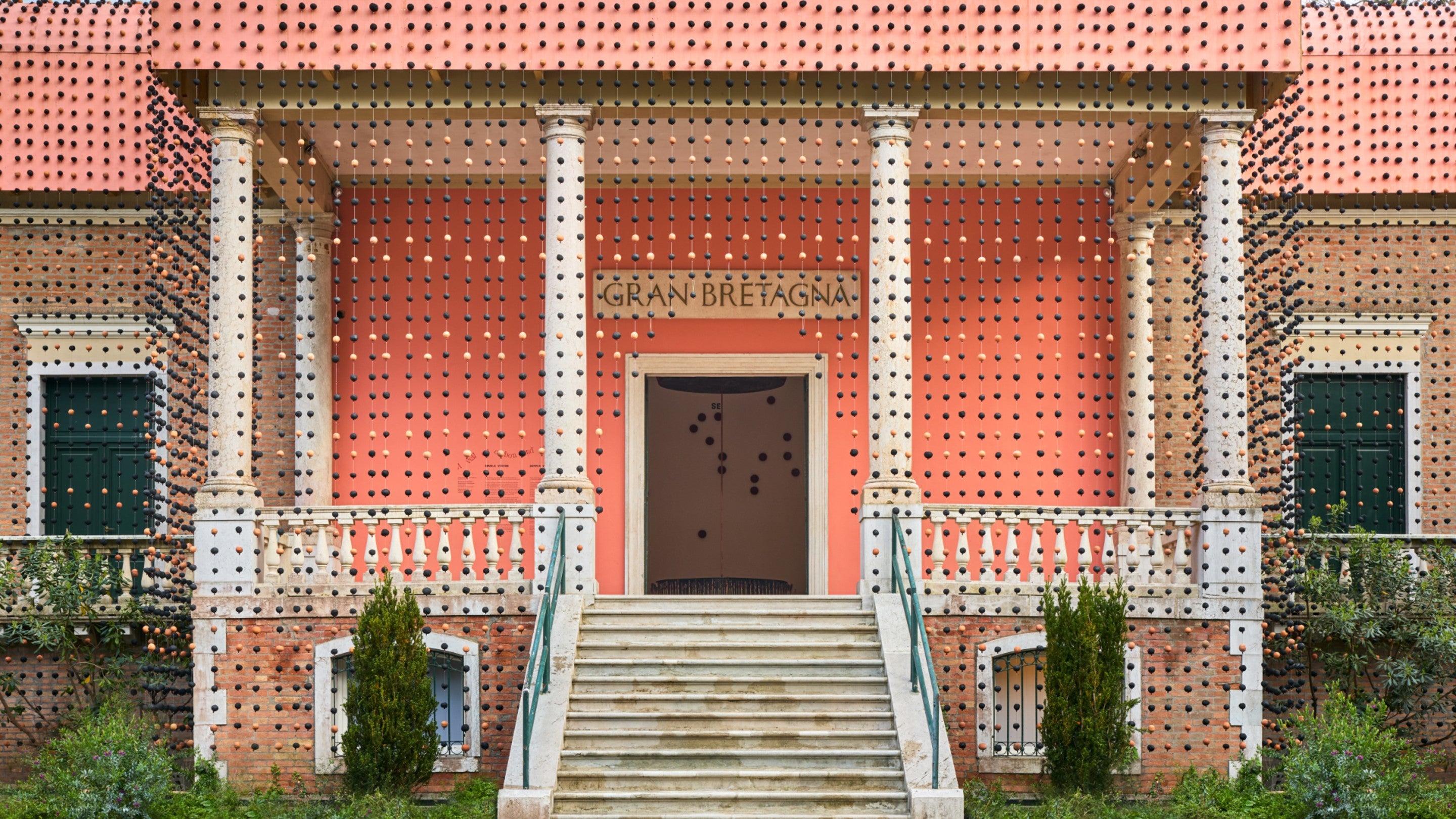 Black and white clay beads hang from the front of a stepped building. Above the entrance door are the words 'Gran Bretagna'e