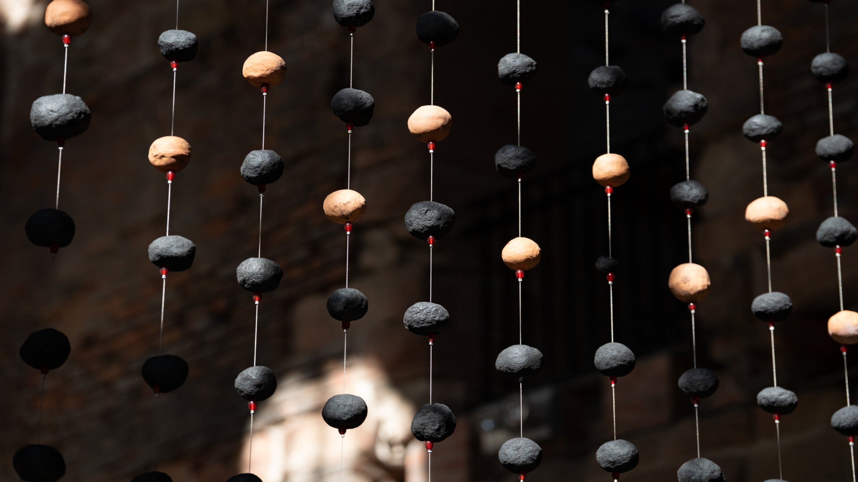 Strings of black and earth coloured clay beads are suspended on strings. The background is dark.