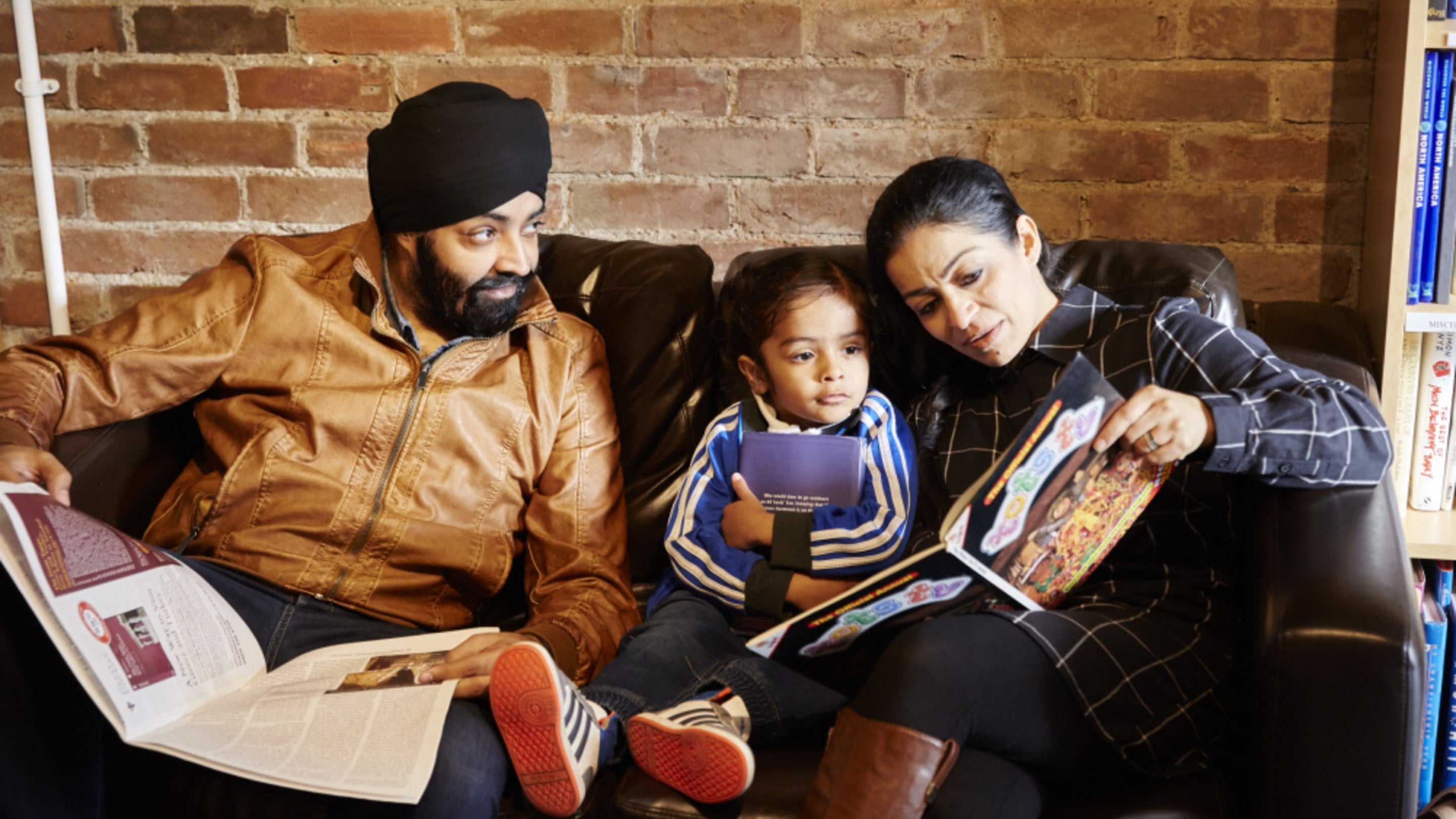A family is sitting on a sofa looking at books together