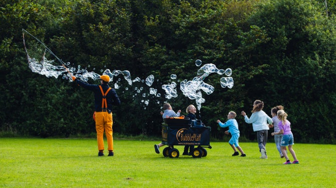 Children chasing giant bubbles on a large grassed area
