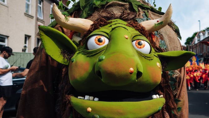 A close up of the face of an extra-large, life-size green puppet's face with horns