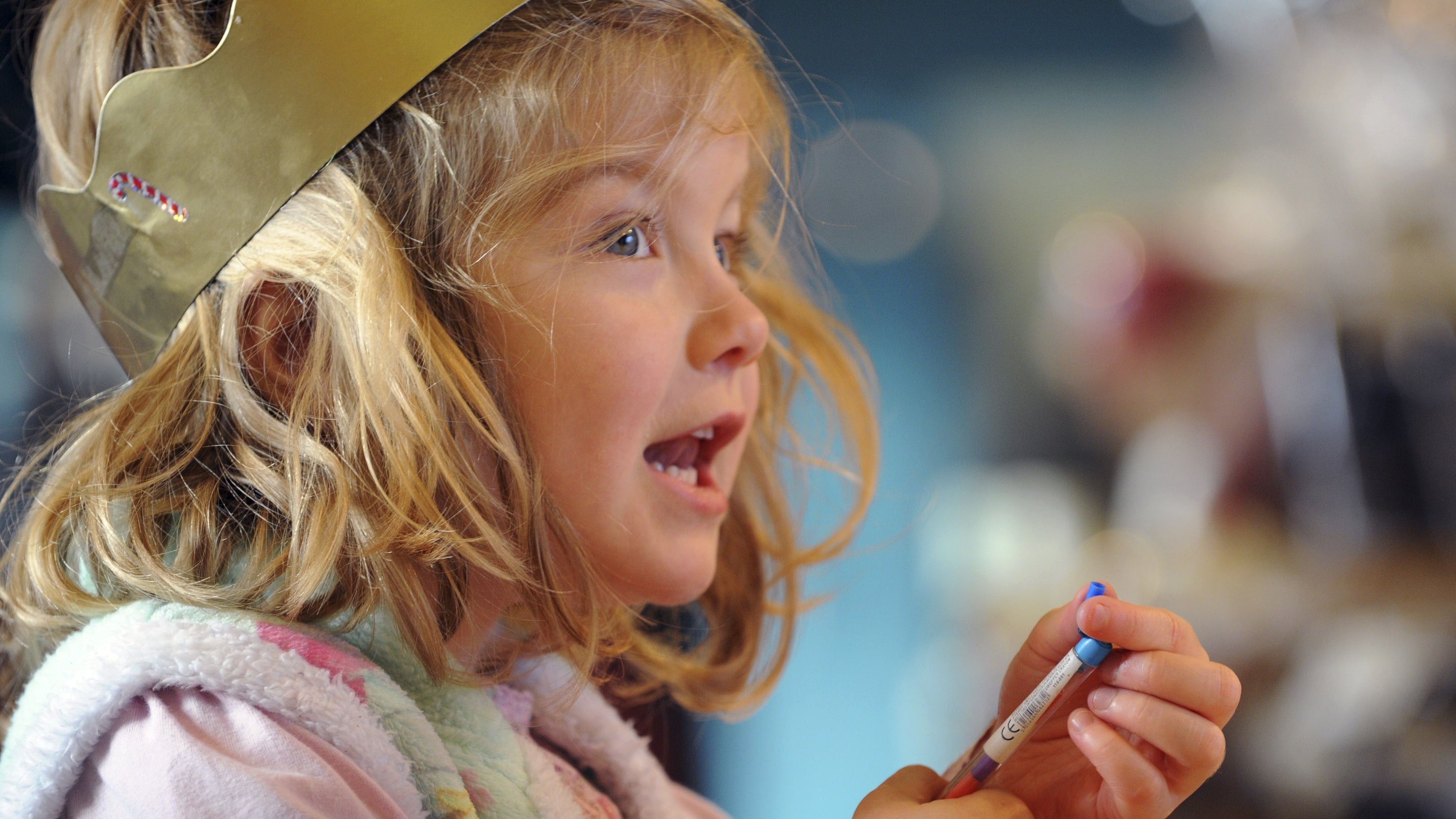 Close up of a smiling child wearing a gold paper crown and holding a coloured pencil
