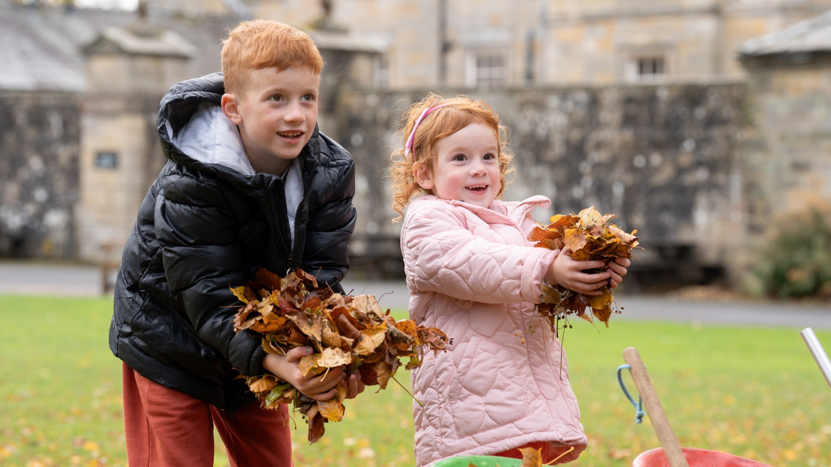 Two children smiling holding up piles of autumn leaves.