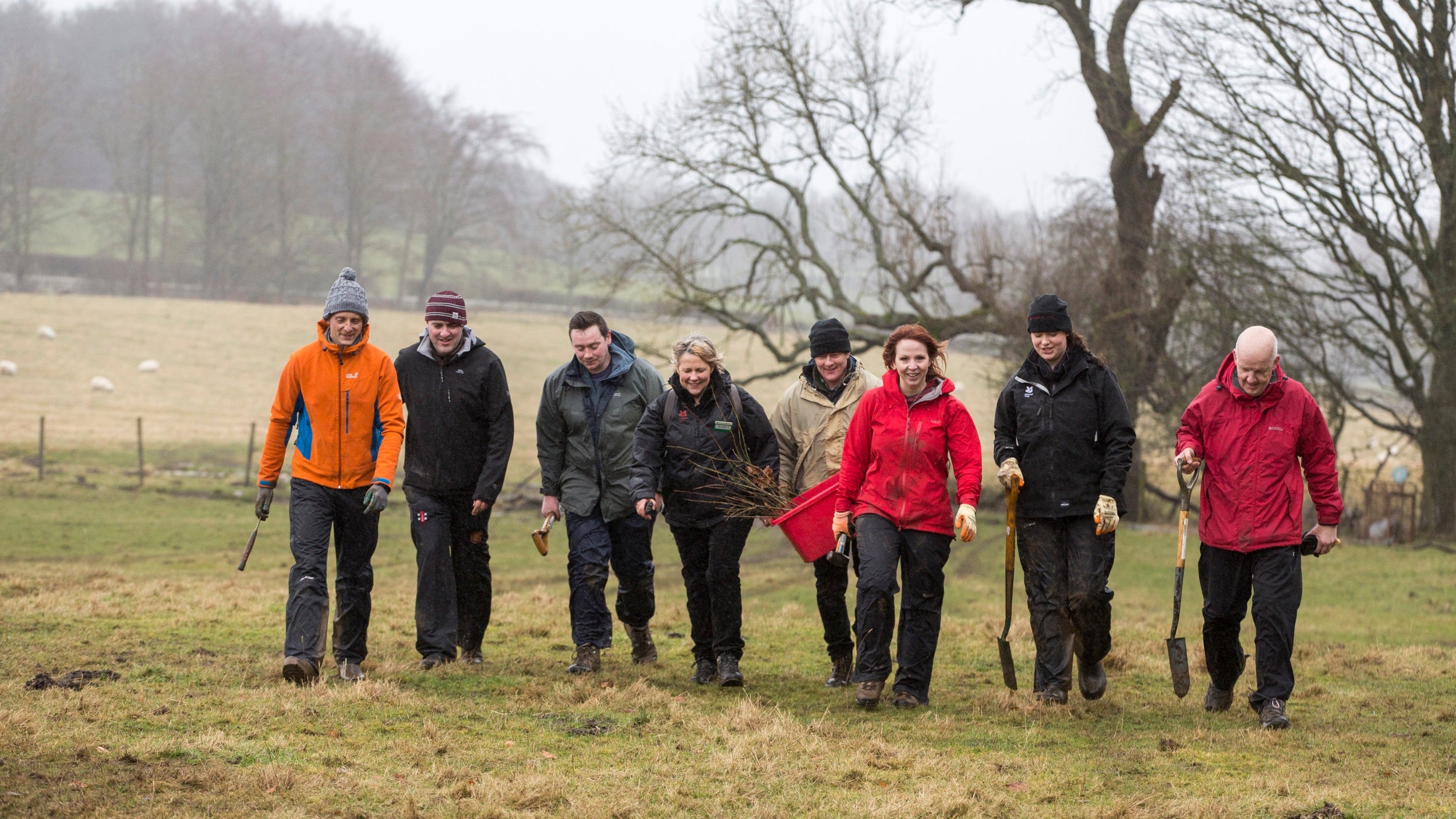 Group of people in winter work gear, walking across field while carrying tools