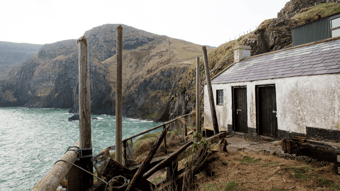 The crane on Carrick-a-Rede island, a relic of the island's fishing heritage, positioned near the Fisherman's Cottage, overlooking steep grassy cliffs and the Atlantic Ocean