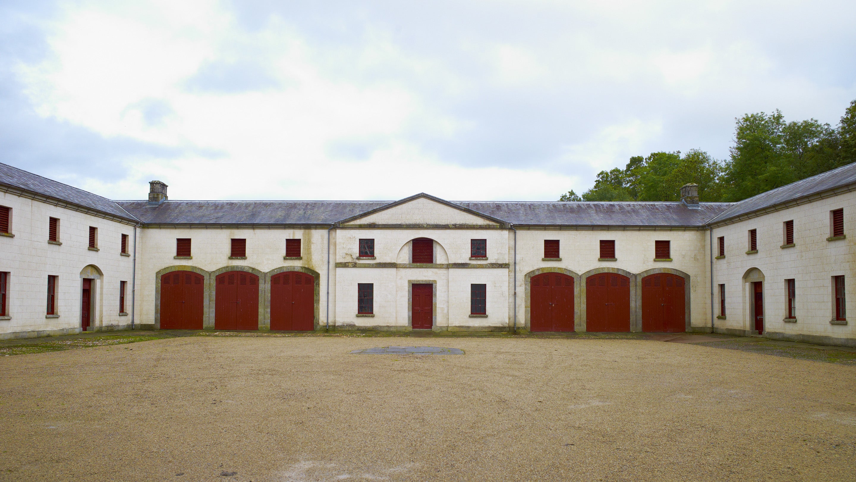 Wide shot of a large block of stables. The six stable doors, three either side of an entrance, are closed and painted red.