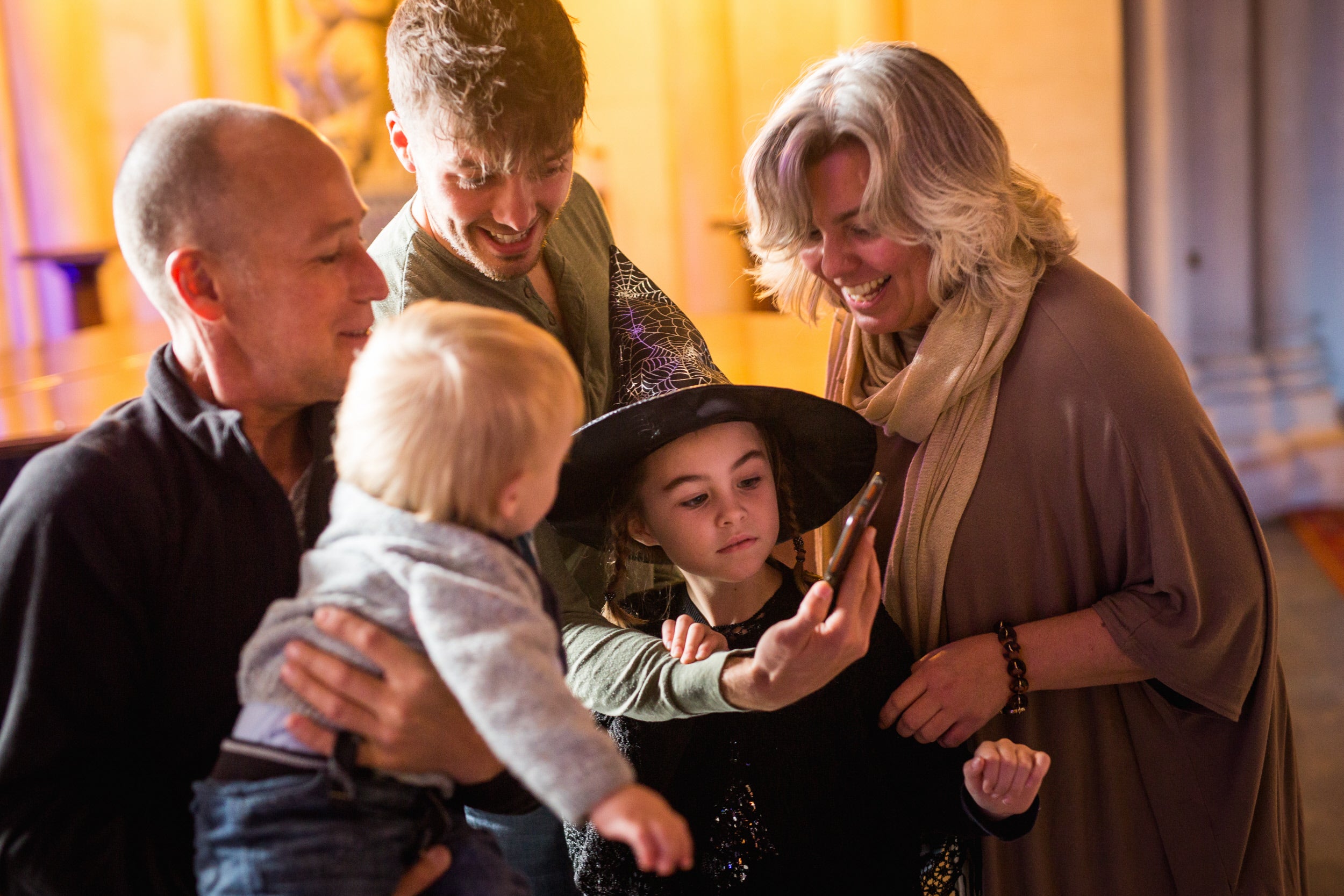 Family, including girl dressed as witch, laughing at a phone.