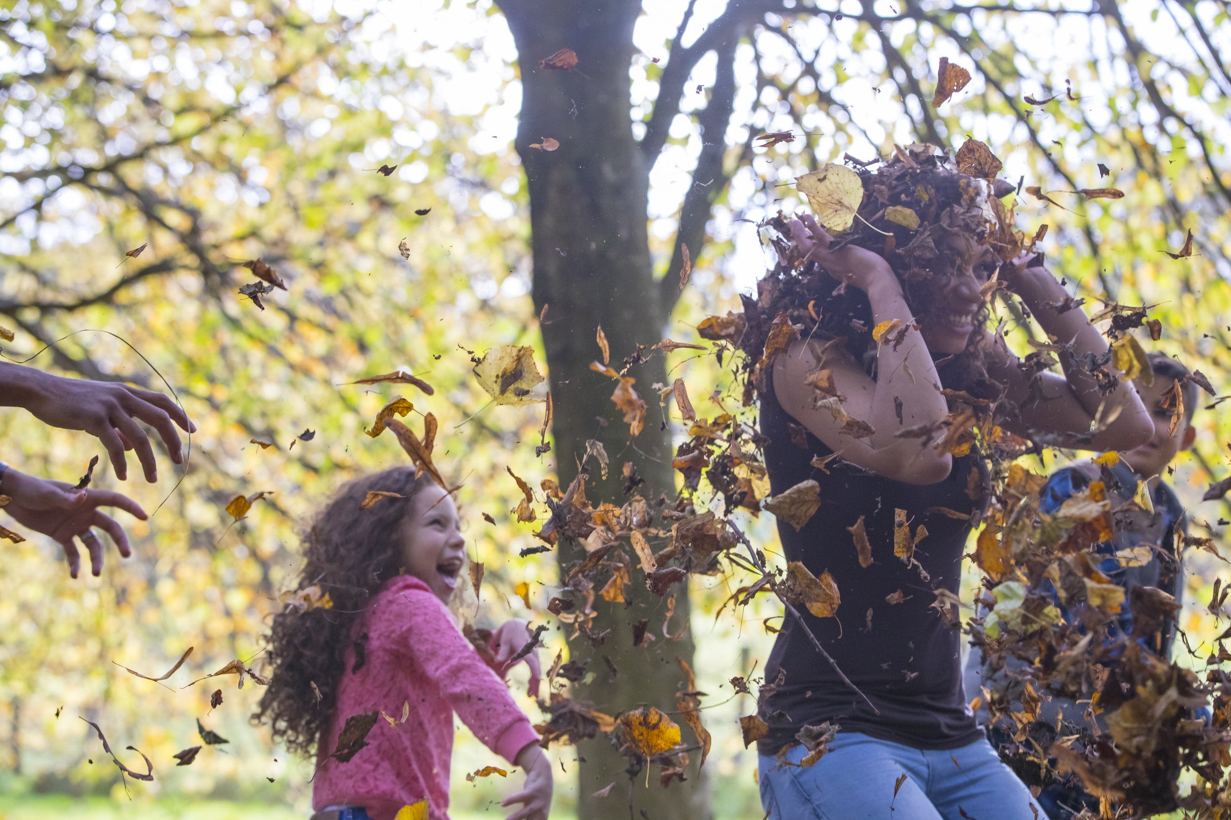 Little girl throwing fallen leaves on her mum
