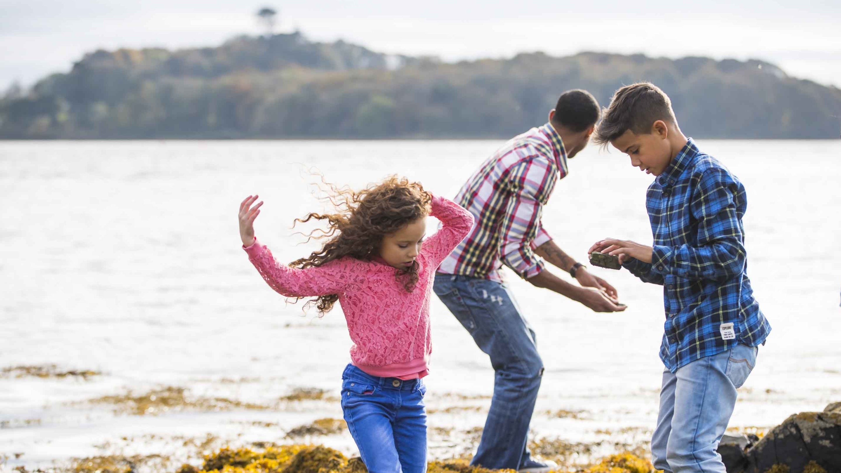 An adult is about to skim a stone on Strangford Lough at Castle Ward, County Down, while two children explore the shoreline.
