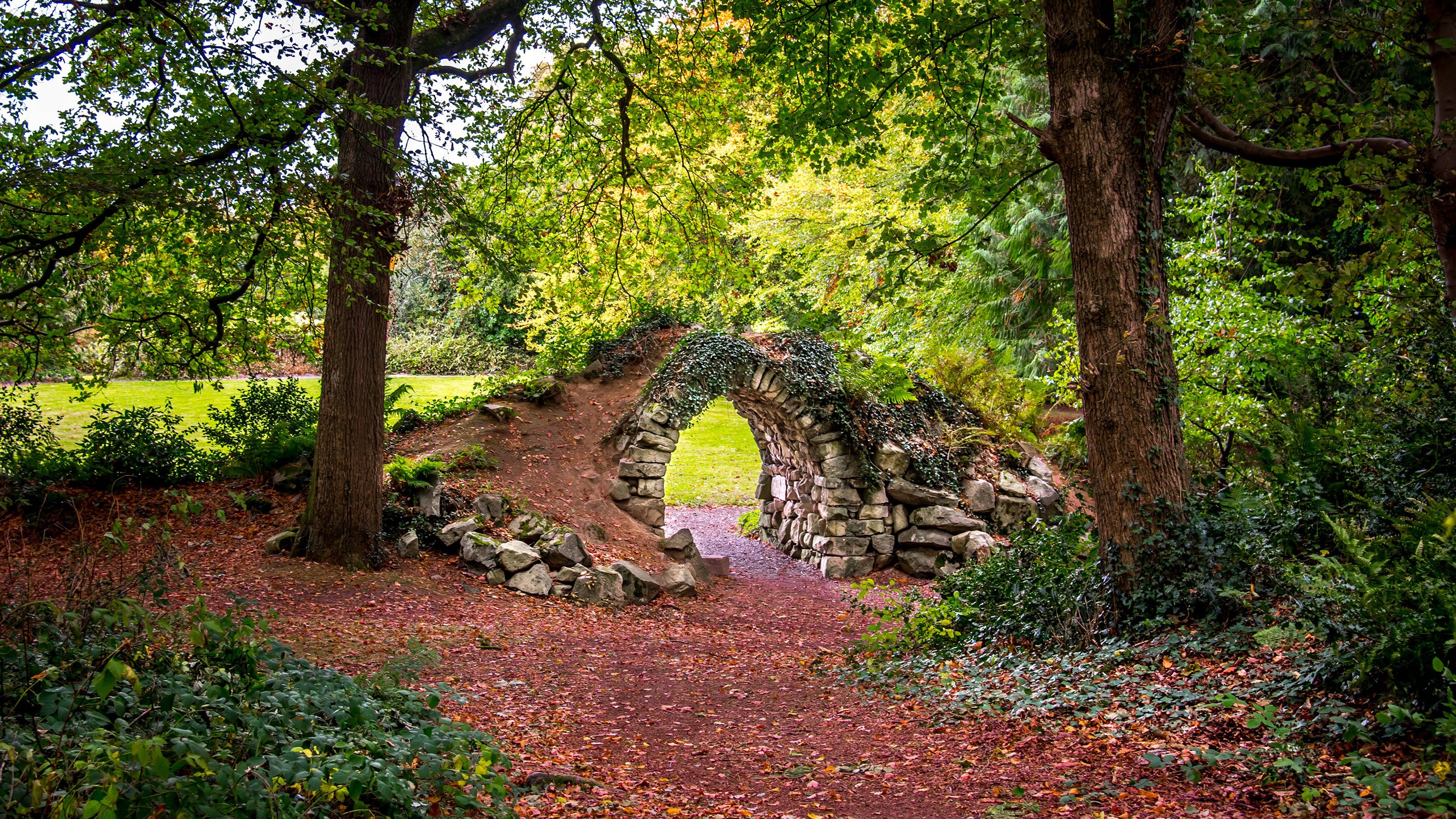 Looking from the trees a path leads through and over a small stone arch