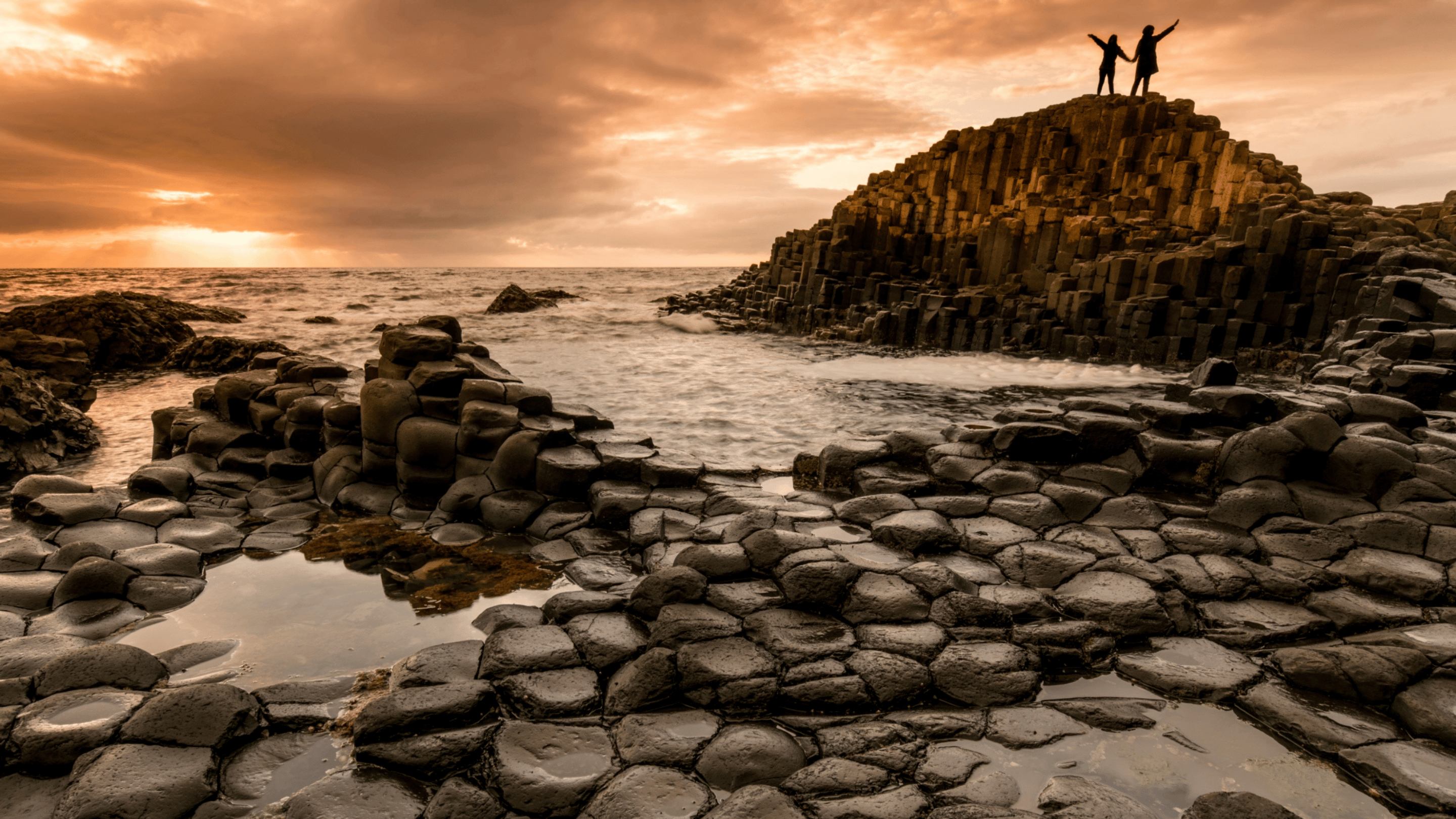 Two visitors standing on top of the Giant's Causeway basalt columns, overlooking the Atlantic