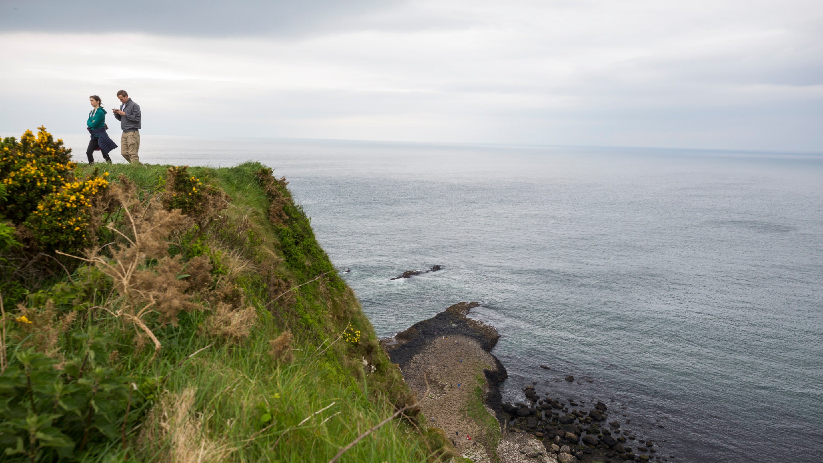 Two people standing on top of a cliff with the sea in the background