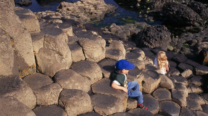 A boy and a girl sitting on the unusual rocks on the Giant's Causeway, County Antrim, Northern Ireland