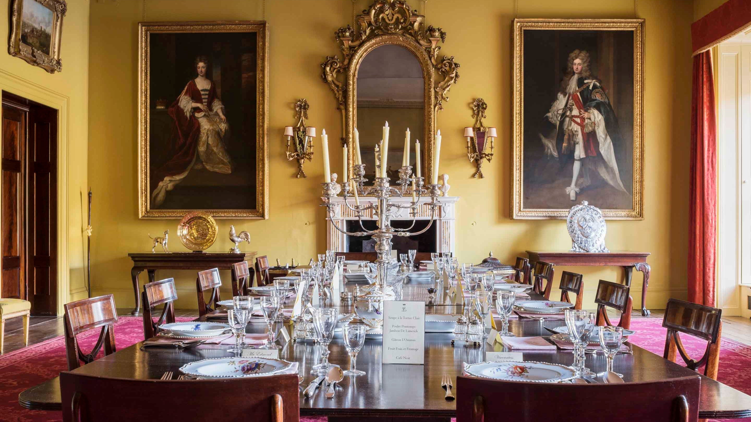 The yellow Dining Room at Mount Stewart with a large table setting and framed portraits and mirrors on the wall