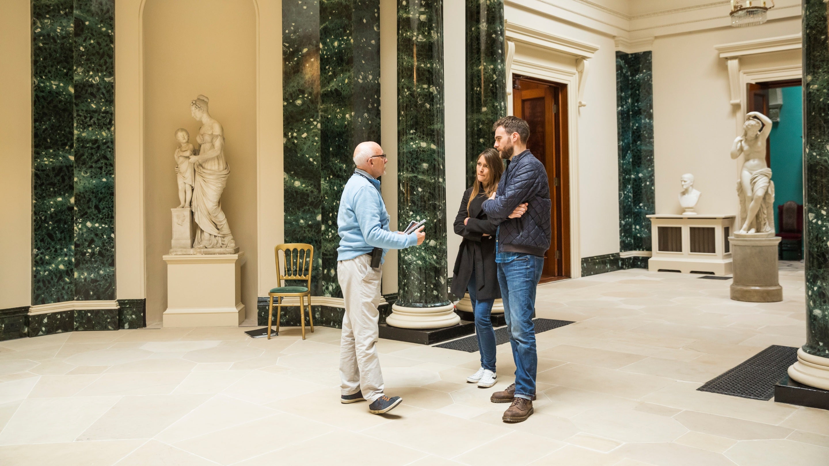 Volunteer room guide speaking with visitors in the Central Hall at Mount Stewart, County Down