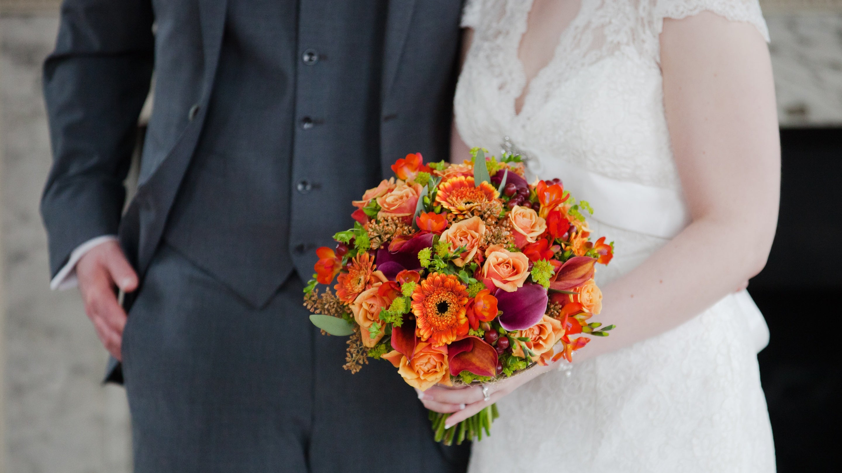 A groom stands next to a bride holding a bouquet of flowers.