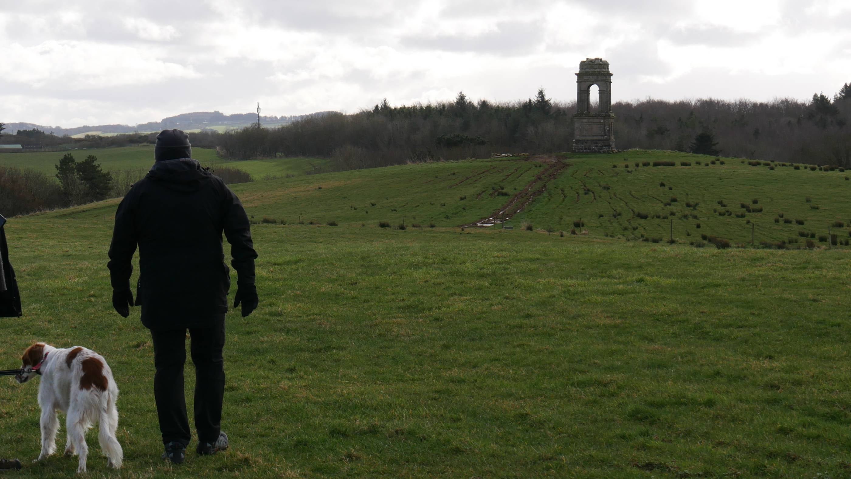 An image of a man with a dog looking out at the Mausoleum from Downhill House.