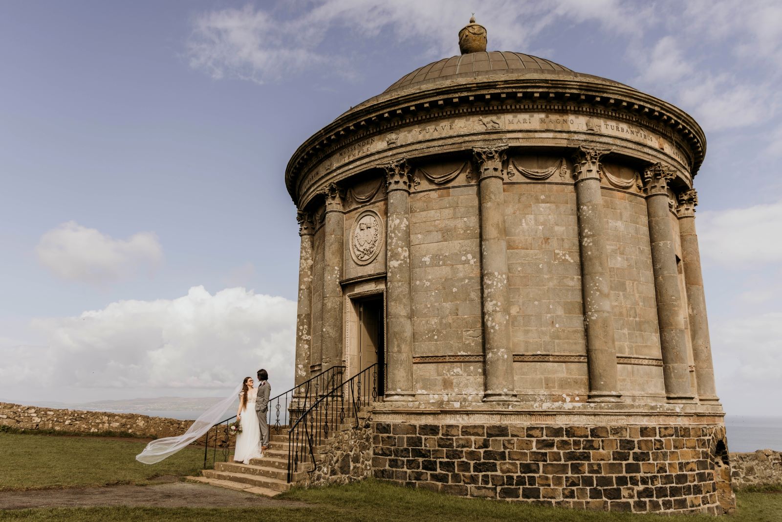 An image of a bride and groom standing on the steps of Mussenden Temple.